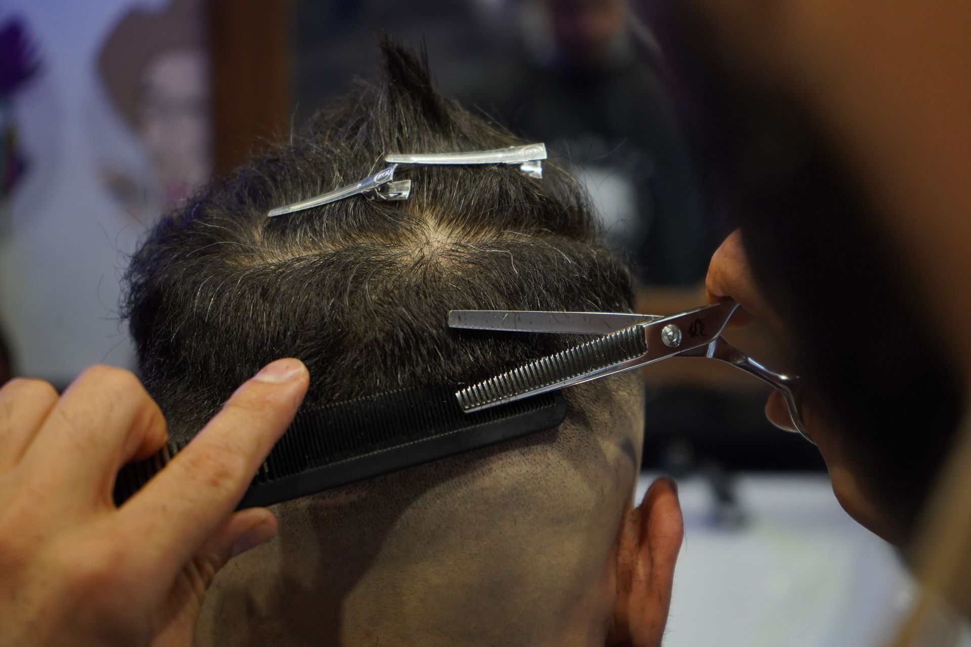Close-up of a barber skillfully cutting a customer's hair with scissors and a comb indoors.